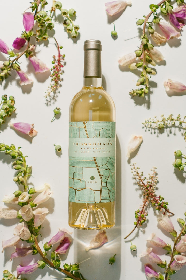 A bottle of Cross Roads Cellars Sauvignon Blanc wine, styled in a flat lay with pink and white flowers on a white background.