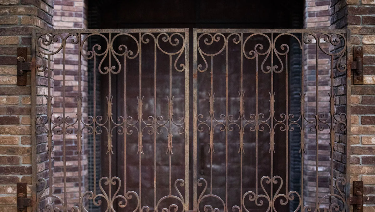 Decorative wrought iron gate with ornate scrollwork and vertical bars, installed in a brick doorway.